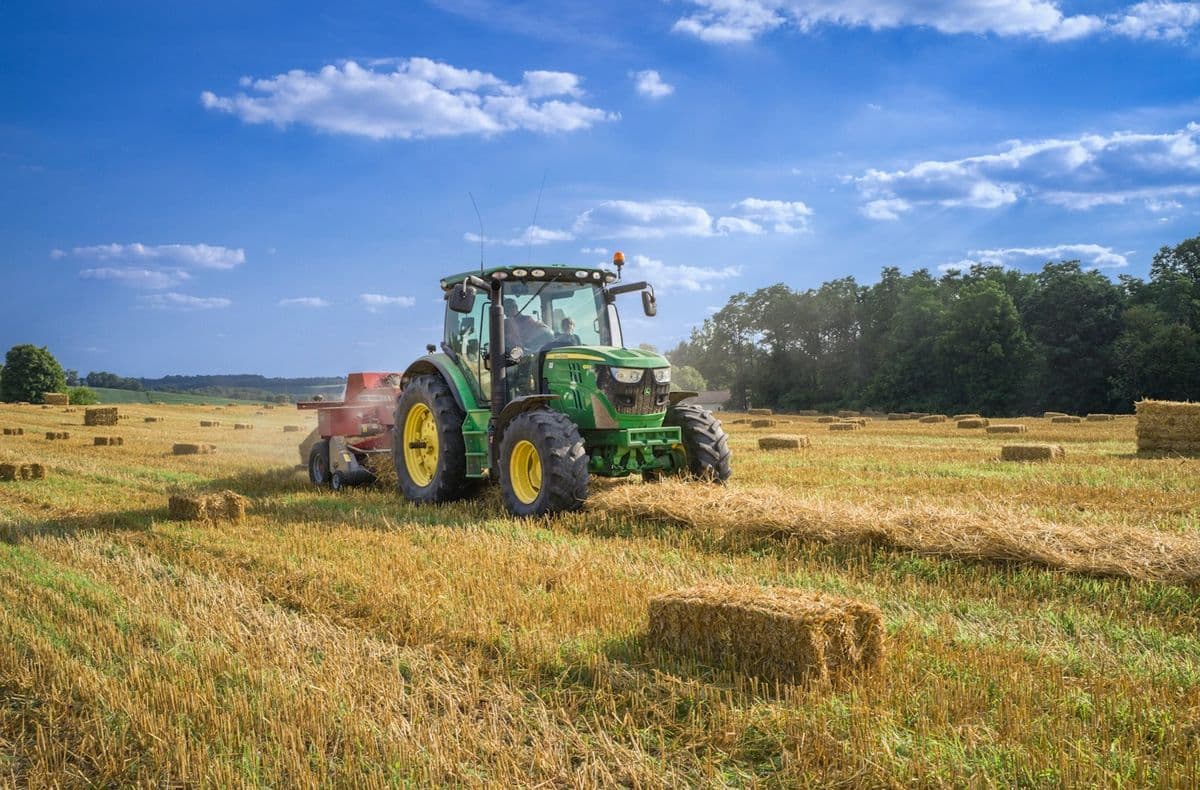 Tractor verde trabajando en un campo con fardos de heno bajo un cielo azul